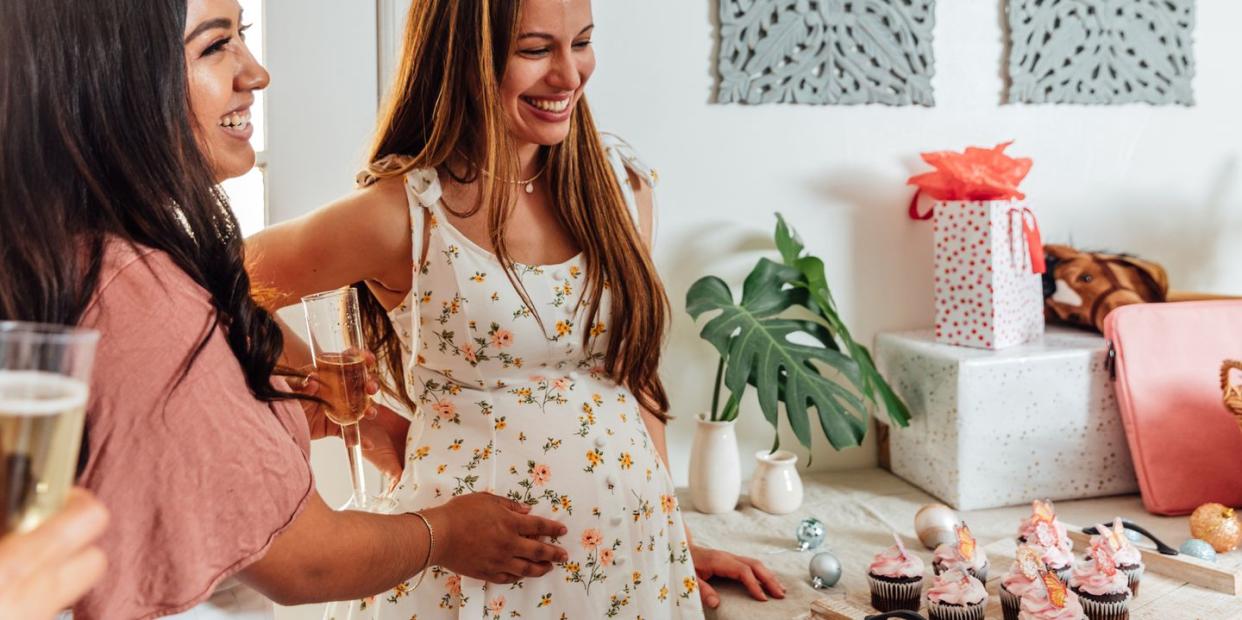 woman touching pregnant belly in front of table at baby shower with gifts and cupcakes