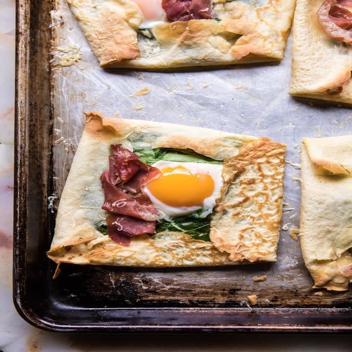 Crepes topped with ham and eggs on a sheet pan.
