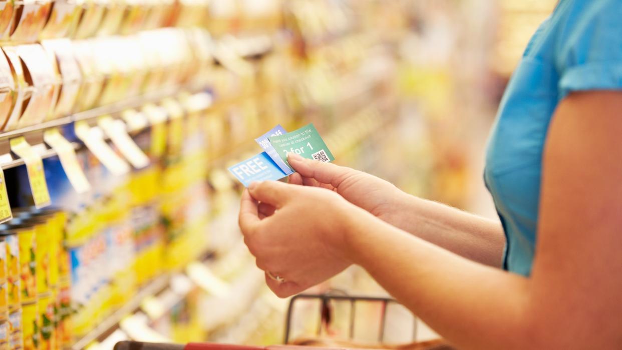 Woman In Grocery Aisle Of Supermarket With Coupons