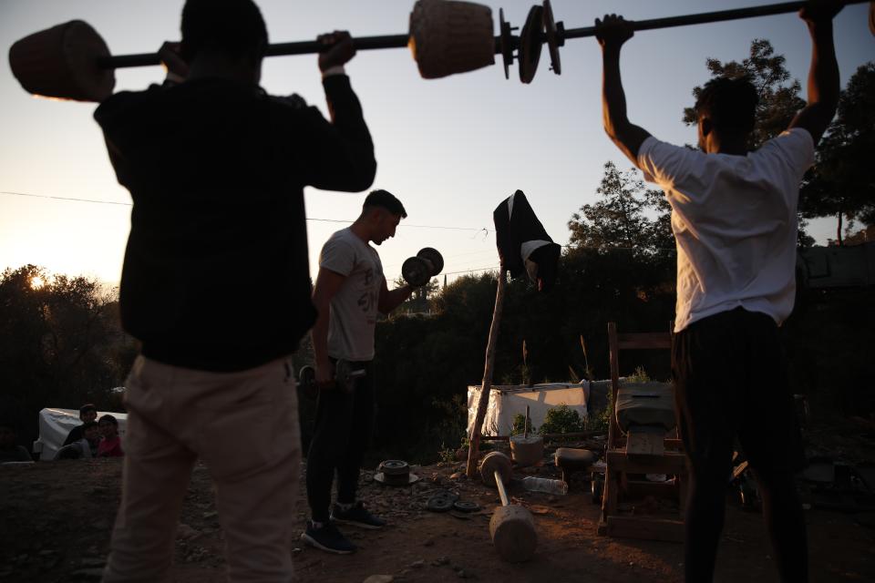 Migrants lift weights at a makeshift gym outside the perimeter of the overcrowded refugee camp at the port of Vathy on the eastern Aegean island of Samos, Greece, Tuesday, Feb. 23, 2021. On a hill above a small island village, the sparkling blue of the Aegean just visible through the pine trees, lies a boy’s grave. His first ever boat ride was to be his last - the sea claimed him before his sixth birthday. His 25-year-old father, like so many before him, had hoped for a better life in Europe, far from the violence of his native Afghanistan. But his dreams were dashed on the rocks of Samos, a picturesque Greek island almost touching the Turkish coast. Still devastated from losing his only child, the father has now found himself charged with a felony count of child endangerment. (AP Photo/Thanassis Stavrakis)
