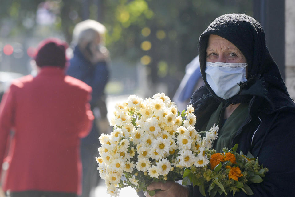 An elderly flower vendor wears a face mask for protection against COVID-19 infection in Bucharest, Tuesday, Oct. 20, 2020. Local authorities imposed the use of face masks in all public spaces, indoors and outdoors, closed schools, restaurants, theatres and cinemas after the rate of COVID-19 infections went above 3 cases per 1000 inhabitants in the Romanian capital Bucharest. (AP Photo/Andreea Alexandru)