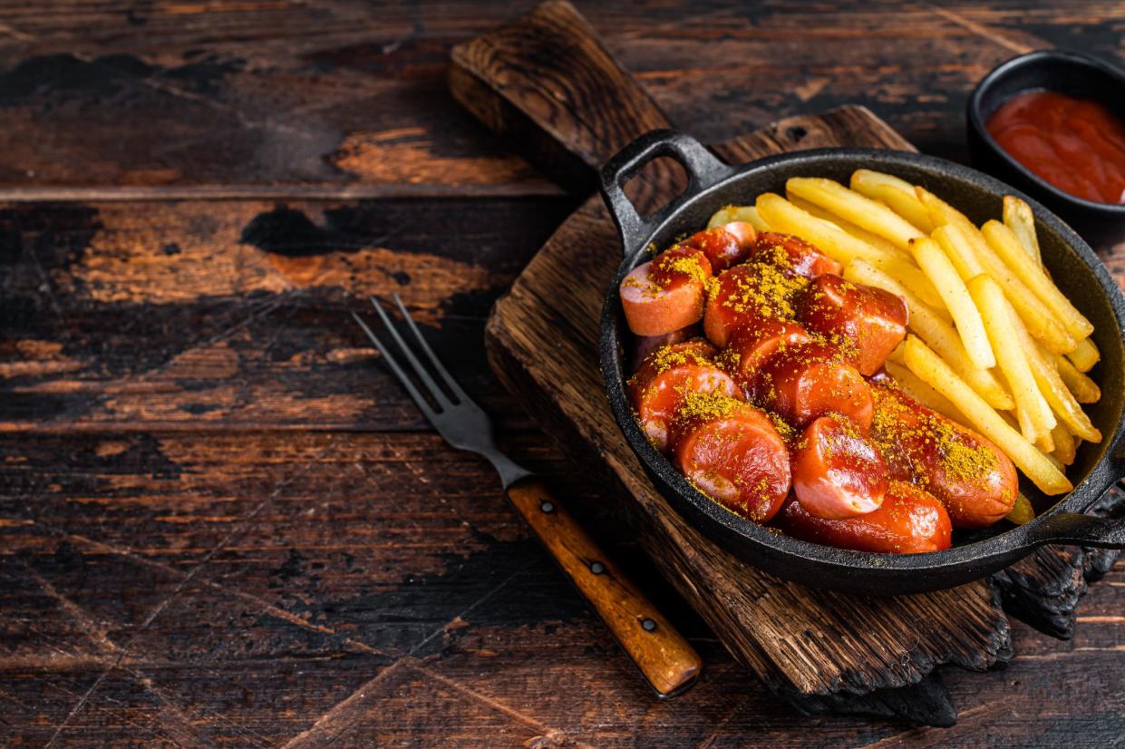 Currywurst street food meal, Curry spice on wursts served French fries in a pan. Dark wooden background. Top view. Copy space.