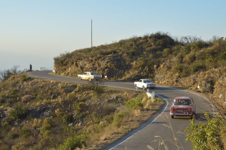 Cae la tarde en la Cuesta del Portezuelo y tres coches toman una de las últimas curvas en ascenso previas a la abrupta bajada hacia San Fernando del Valle de Catamarca, que está a su izquierda.