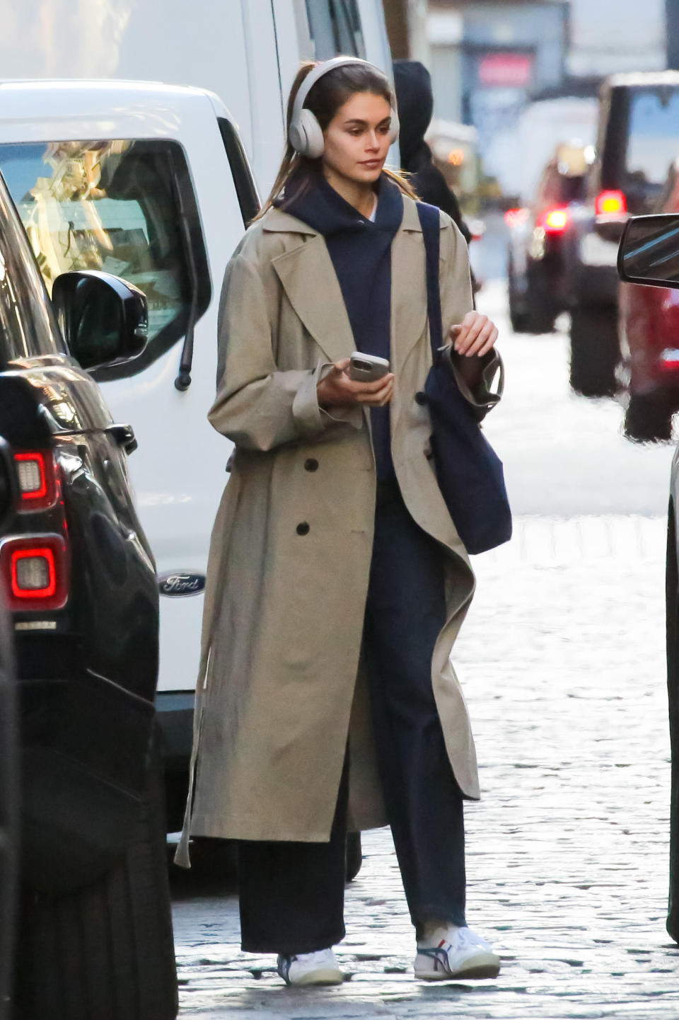 kaia gerber wearing a trench coat and onitsuka sneakers with her AirPods in New York City