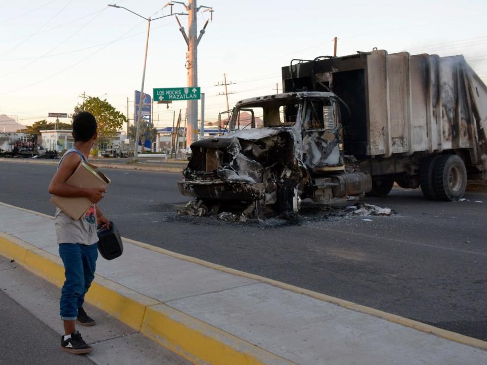 A man passes by a burned truck during an operation to arrest the son of Joaquin 'El Chapo' Guzman, Ovidio Guzman, in Culiacan, Sinaloa state, Mexico, on Thursday. The pre-dawn operation Thursday set off gunfights and roadblocks across the western state’s capital.  (Juan Carlos Cruz/AFP/Getty Images - image credit)