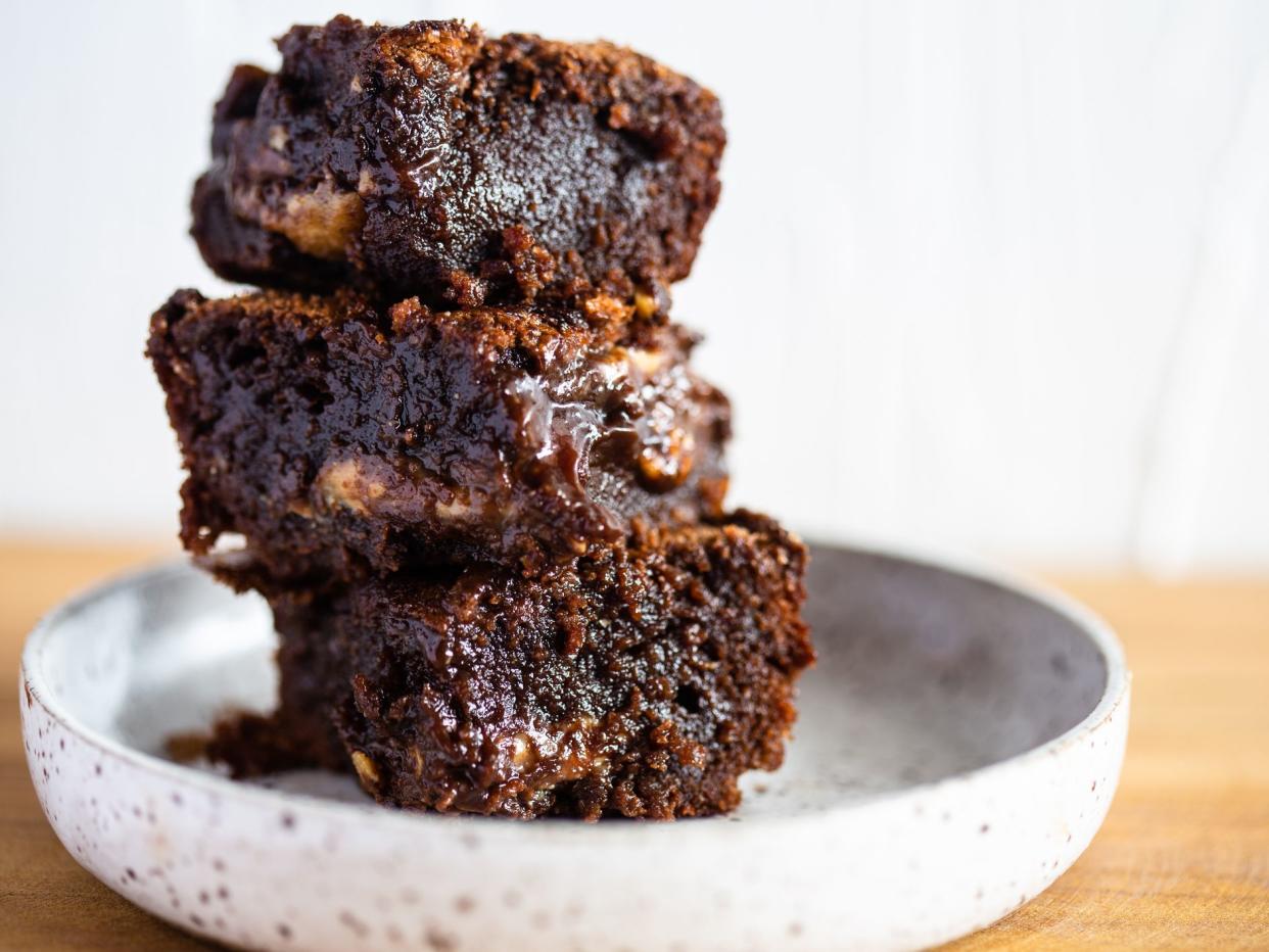 Pile of moisty chocolate brownie on a white ceramic and wood table.