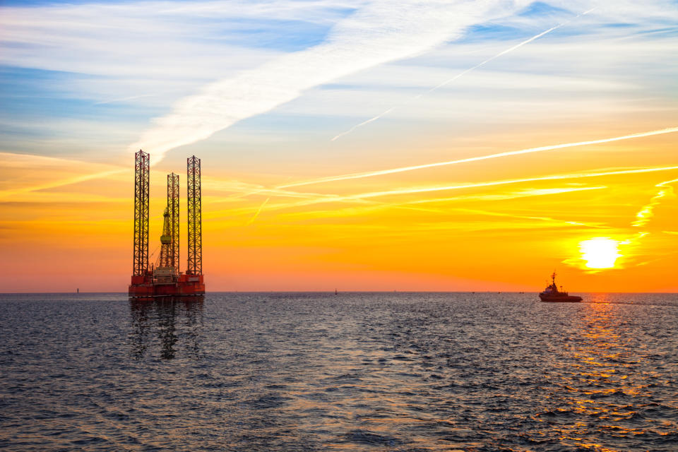 An offshore rig at sunset with a ship in the background.