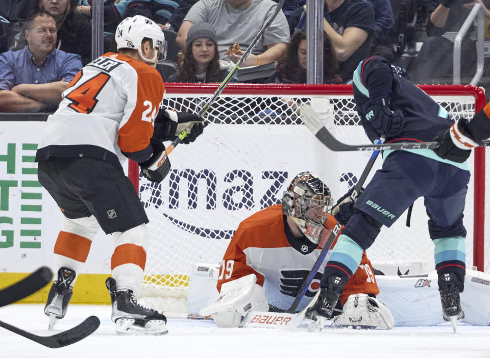 Seattle Kraken right wing Jordan Eberle, right, digs for the puck on a shot blocked by Philadelphia Flyers goaltender Carter Hart (79) with Flyers defenseman Nick Seeler, left, looking on during the second period of an NHL hockey game, Friday, Dec. 29, 2023, in Seattle. (AP Photo/John Froschauer)