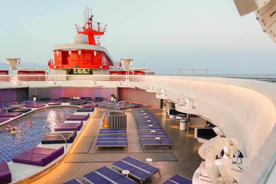 A pool seen from the top deck of a cruise ship with purple and blue pool chairs.