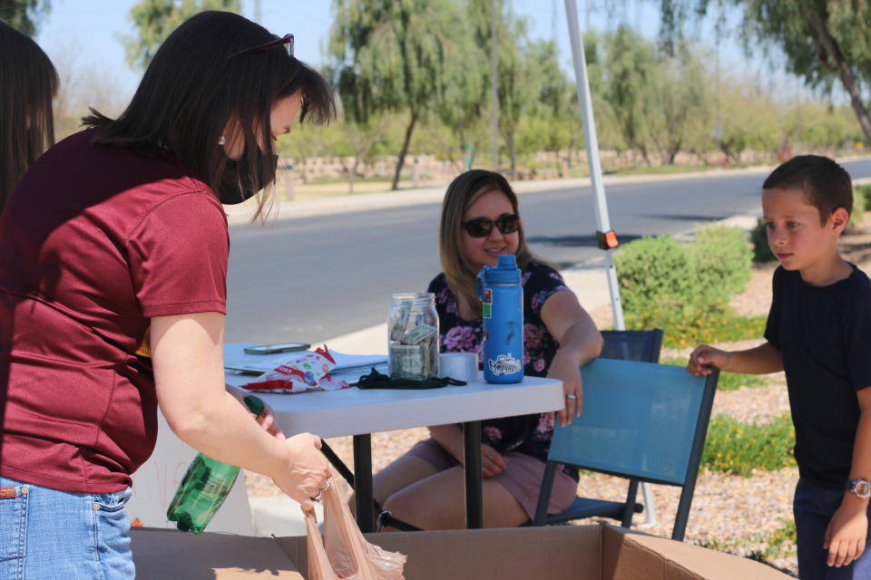 Dylan Pfeifer watches as neighbors add bags of canned food to his collection box during a food drive on Saturday, April 3, 2021, in Chandler, Ariz. Pfeifer hosted his third food drive since October in response to the coronavirus pandemic from his home in Chandler.He said he is planning his next one in June, when summer vacation begins. (AP Photo/Cheyanne Mumphrey)