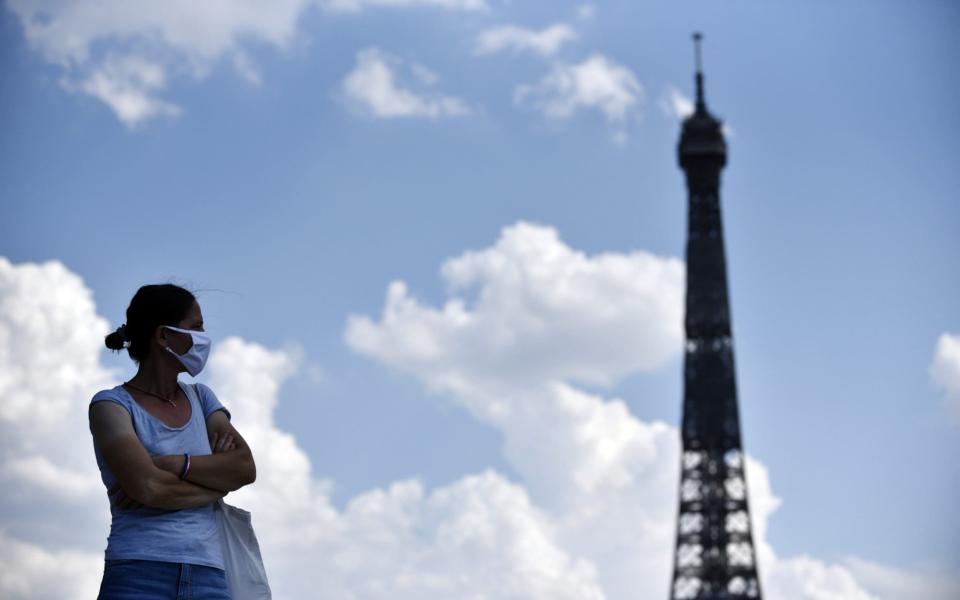 A woman wears a face mask in front of the Eiffel Tower in Paris, France - Shutterstock