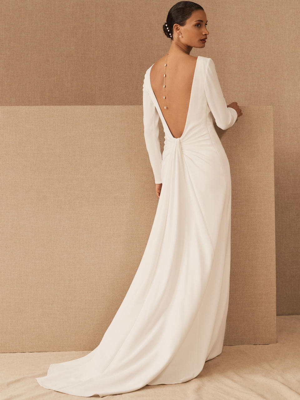 <p>With tailored ripples at the waist, a romantic sash, and plunging back, the "Maven" gown from <a href="https://www.bhldn.com/" rel="nofollow noopener" target="_blank" data-ylk="slk:BHLDN;elm:context_link;itc:0;sec:content-canvas" class="link ">BHLDN</a>'s latest series—this dress was designed in partnership with Tadashi Shoji—is both traditional and subtly daring. Take the model's lead and accessorize with a trail of pearls down your spine.</p>