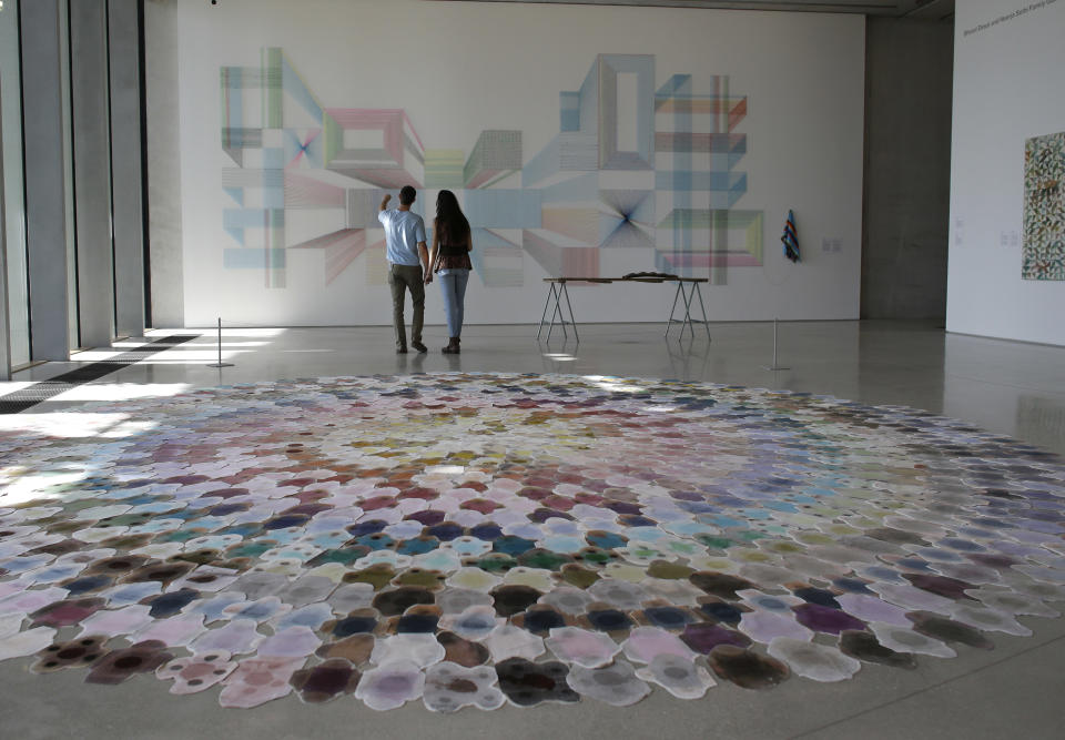 In this Thursday, Dec. 12, 2013 photo, museum goers look at a piece on the wall titled "Wake and Wonder " by artist Adrian Esparza, who literally deconstructs the cliche Mexican serape and repurposes it into a vast, geometric weaving, at the Perez Art Museum Miami, in Miami. The museum, called the PAMM by locals, opened in December and is becoming a must-see destination for tourists and locals alike with its eclectic and provocative collection. (AP Photo/Lynne Sladky)