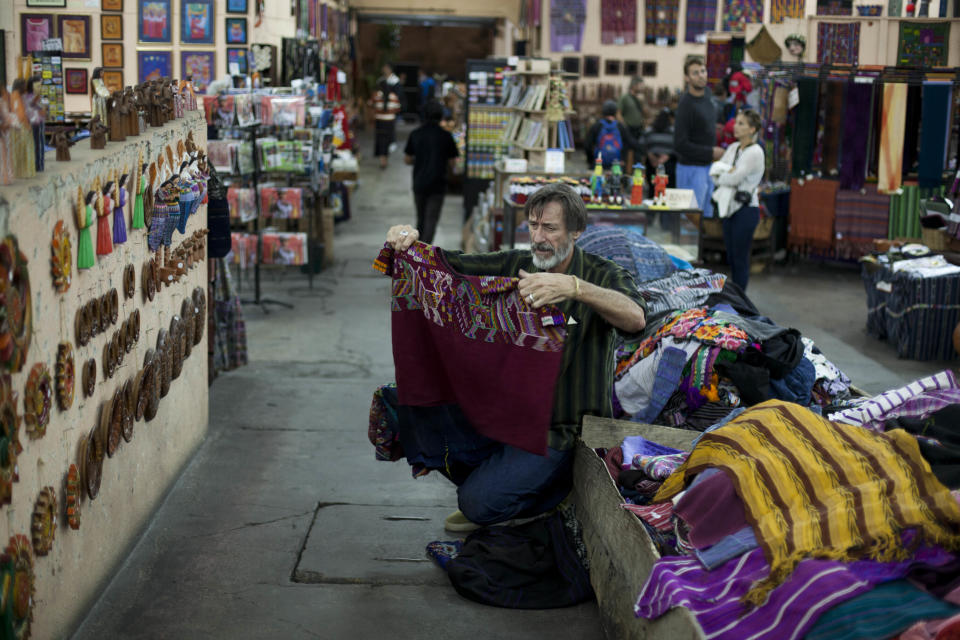 In this Nov. 14, 2013 photo, a tourist buys indigenous textiles at a market in Antigua, Guatemala. In recent months, this UNESCO World Heritage Site has seen the troubles of the outside world threaten the town’s backpacker charm. (AP Photo/Luis Soto)