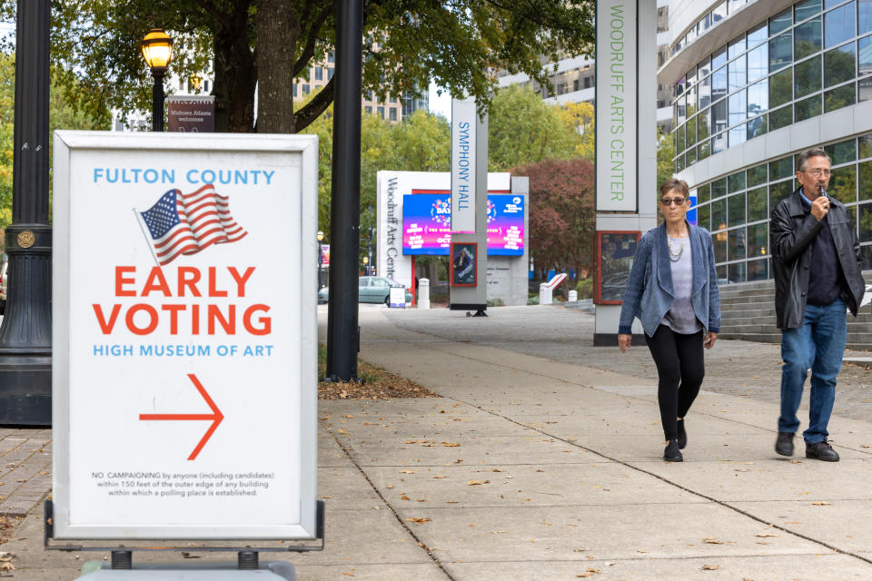 Two people on a sidewalk approach a sign that reads: Fulton County early voting High Museum of Art.
