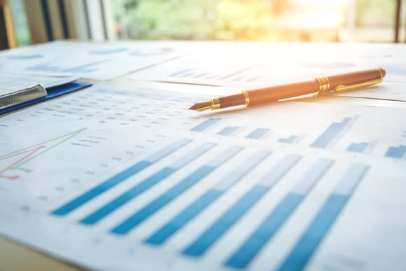 Papers showing charts and graphs are spread out on a desktop, with a pen sitting on top of them.