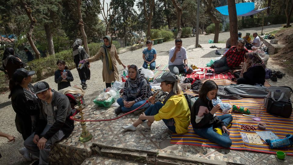 An Iranian young woman puffs on a hookah as she and her family sit together in a park in northern Tehran during the day of Sizdah Bedar, also known as Nature's Day, on April 2, 2022.  - Morteza Nikoubazl/NurPhoto/Getty Images