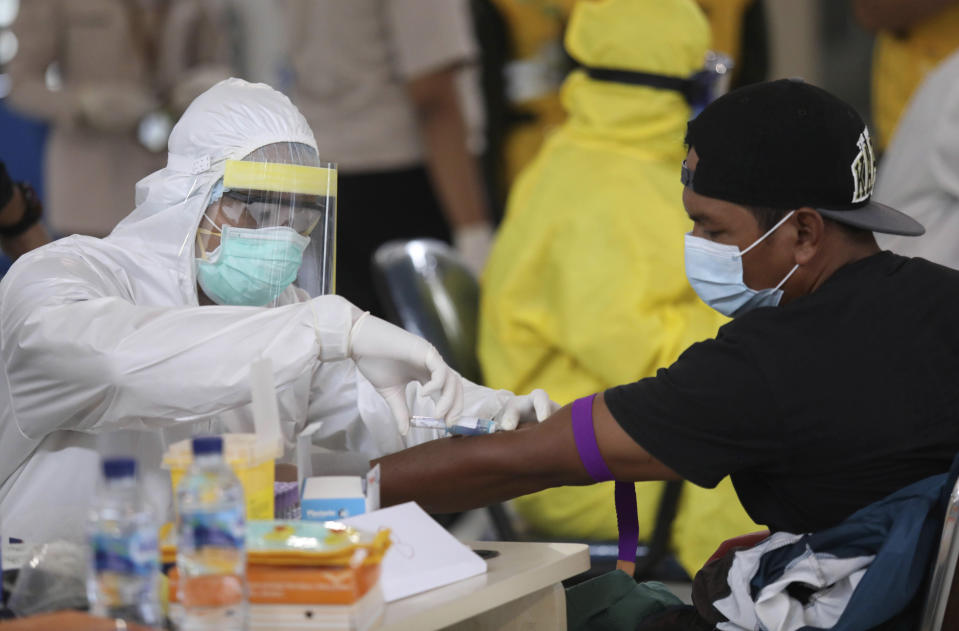 A medical worker collects a blood sample from a man during a test for coronavirus for migrant workers returning from Malaysia in Surabaya, Indonesia, Tuesday, April 7, 2020. The new coronavirus causes mild or moderate symptoms for most people, but for some, especially older adults and people with existing health problems, it can cause more severe illness or death. The migrant workers will be quarantined for 14 days before they are allowed to leave for their home villages. (AP Photo/Trisnadi)