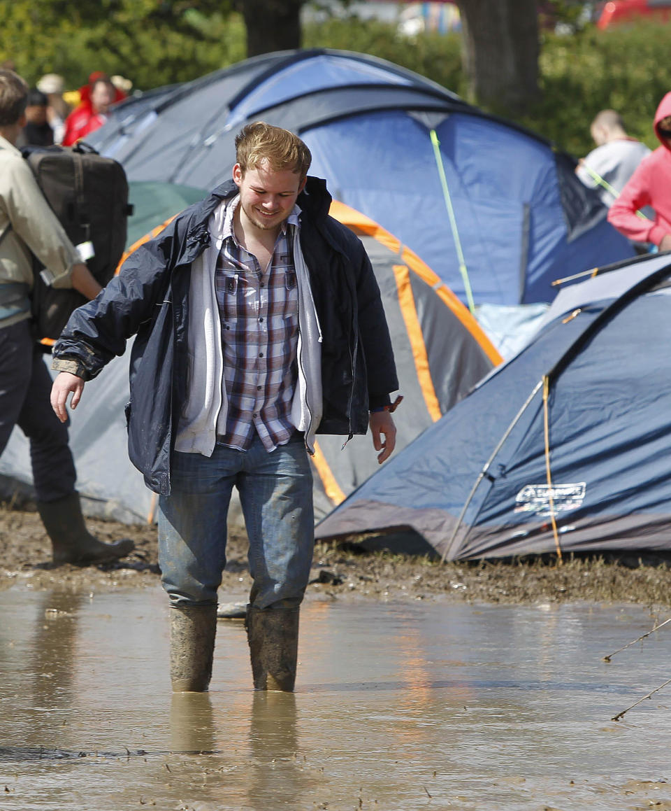 A festival goer walks through the water and mud at the campsite at the Isle of Wight festival on the Isle of Wight England Friday June 22, 2012. Hundreds of music fans have been stranded in their cars overnight after rainstorms caused chaos on travel routes to the Isle of Wight Festival. (AP Photo/Peter Byrne/PA) UNITED KINGDOM OUT