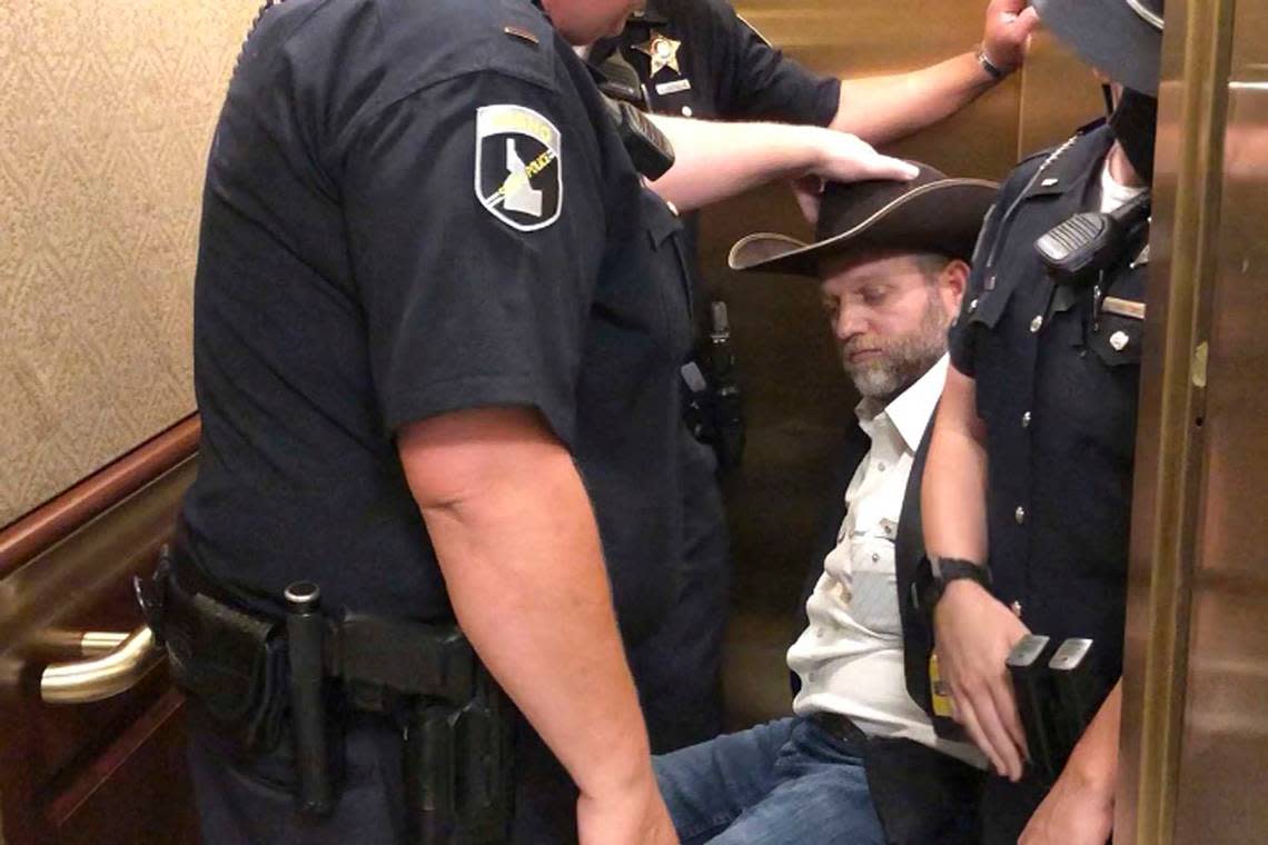 In 2020, Ammon Bundy, rear, was wheeled into an elevator in a chair following his arrest at the Idaho Statehouse in Boise. In 2023, he rolled out of Idaho fleeing legal woes.