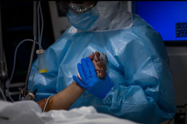 PHOTO: A doctor holds the hand of a COVID-19 patient in critical care in Barcelona's Hospital del Mar the Intensive Care Unit, Spain, Nov. 5, 2020. (Emilio Morenatti/AP, FILE)