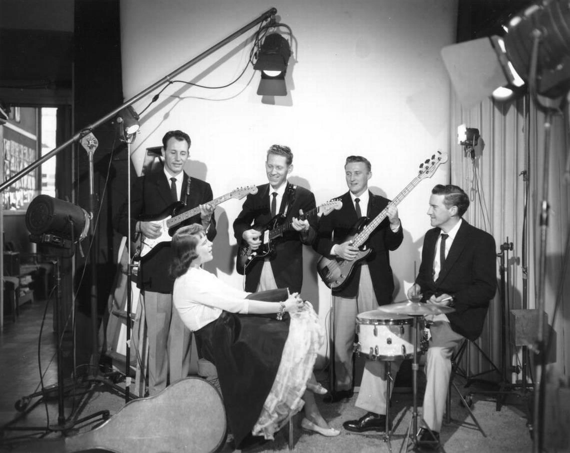 Collection: Richards Studio Collection Series: D126221-14 (Unique: 8878) Date: 04-26-1960 Description: In April 1960, Tacoma originated rock group “The Ventures” posed for a publicity photo with an unidentified woman admirer. Left to right: Nole F. (Nokie) Edwards, Bob Bogle, Don Wilson, Howie Johnson. The most popular and influential instrumental rock band of all time got its start at the Blue Moon in Tacoma. At that time, band originators Bogle and Wilson were playing as a rock duo “The Versatones.” They wooed lead guitarist Nokie Edwards and drummer Skip Moore (later replaced by Johnson) away from country performer Buck Owens to record “Walk, Don’t Run” as The Ventures. From the beginnings of this gold single, they became guitar legends. The Ventures were inducted into the Rock and Roll Hall of Fame in March 2008.