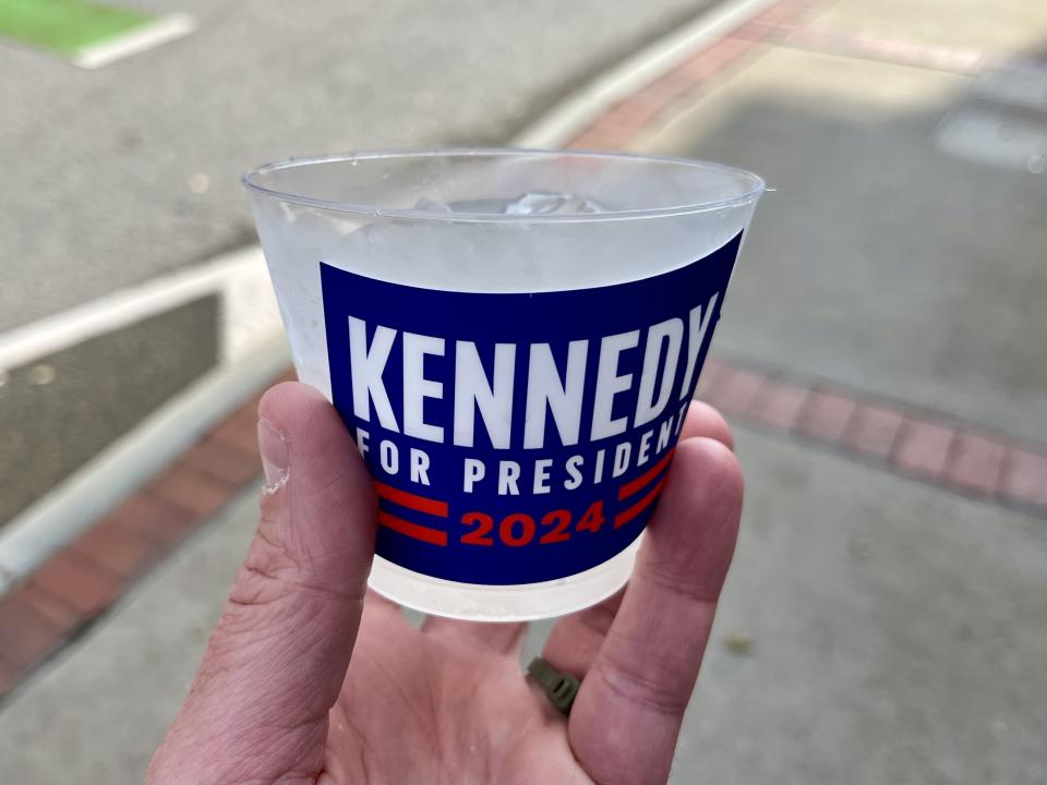 A hand holds a cup of lemonade bearing a sticker that reads: Kennedy for president 2024. 