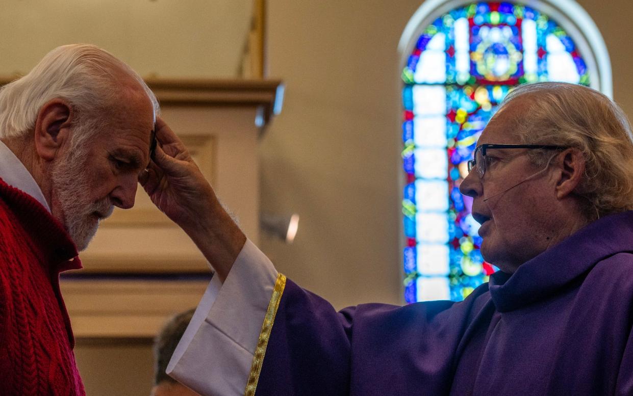 Father John Madden, right, places ashes on a worshipper during Ash Wednesday Mass at St. John’s Catholic Church Wednesday.