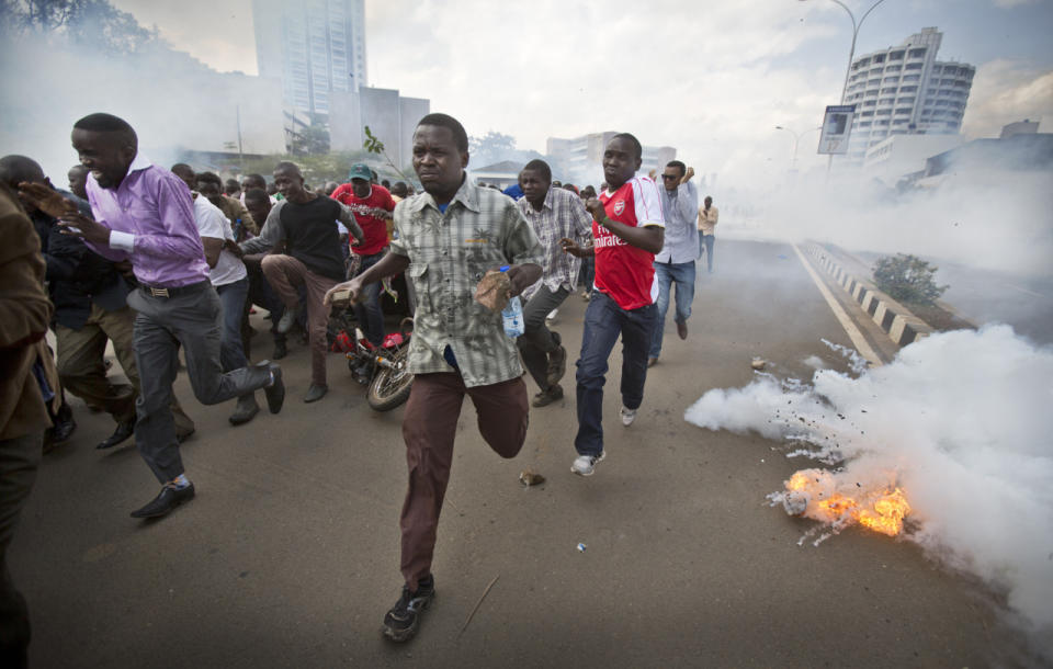 Opposition supporters, some carrying rocks, flee from exploding tear gas grenades fired by riot police, during a protest in downtown Nairobi, Kenya, May 16, 2016. Kenyan police have tear-gassed and beaten opposition supporters during a protest demanding the disbandment of the electoral authority over alleged bias and corruption. (AP Photo/Ben Curtis)