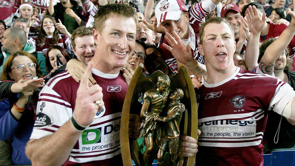 On the left, Steve Menzies poses with the NRL premiership trophy he won with Manly in 2008.