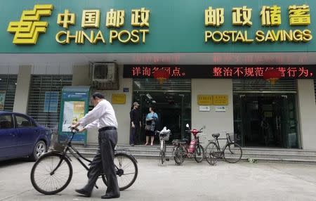 File photo of a man pushing his bicycle past a branch of China Post's Postal Savings Bank of China in Wuhan, Hubei province May 4, 2012. REUTERS/Stringer