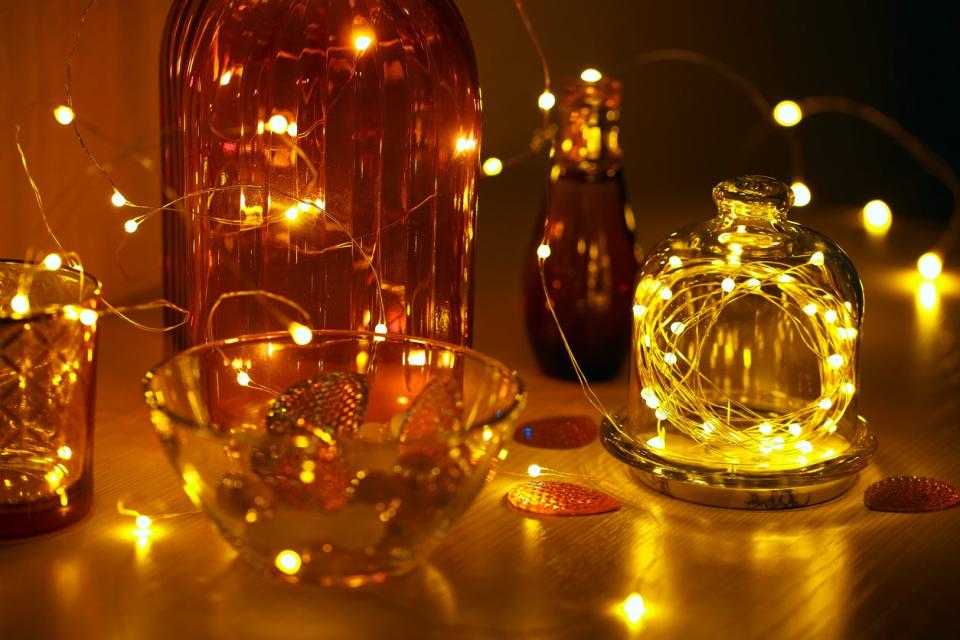 Several-glass-containers-hold-fairy-string-lights-inside-and-are-sitting-on-a-wood-table.