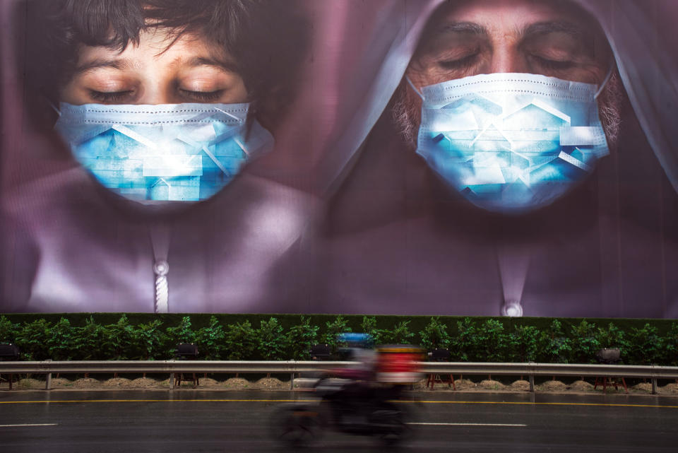 A motorcycle deliveryman rides past a billboard urging people to stay during the coronavirus pandemic in Dubai, United Arab Emirates, Wednesday, April 15, 2020. (AP Photo/Jon Gambrell)