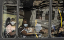 Commuters wearing face masks peer through a bus window during increased restrictions on movements in an effort to curb the spread of the new coronavirus in the Madureira area of Rio de Janeiro, Brazil, Tuesday, May 12, 2020. (AP Photo/Silvia Izquierdo)