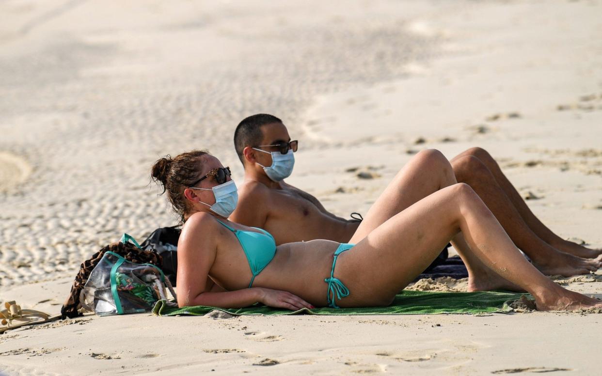 A man and a woman, clad in face masks due to the COVID-19 coronavirus pandemic, lie on the sand by the shore of a beach in the Gulf Emirate of Dubai - KARIM SAHIB/AFP