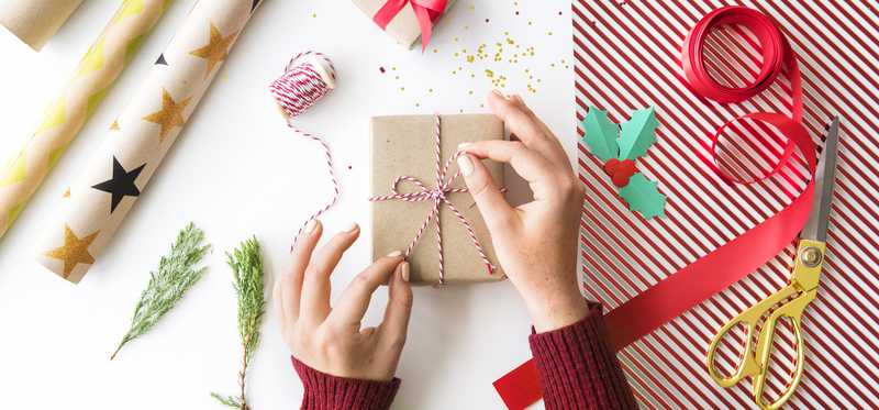 A woman tying a bow on a handwrapped gift.