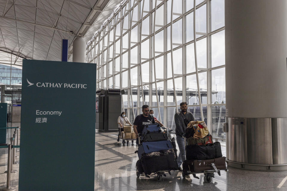 Travelers walk through the departures hall near a sign for Cathay Pacific at Hong Kong International Airport in Hong Kong, on Wednesday, March. 8, 2023. Cathay Pacific Airways Ltd. said it was ready to rebuild as Hong Kong opened up to global visitors, despite reporting wider losses in 2022. (AP Photo/Louise Delmotte)
