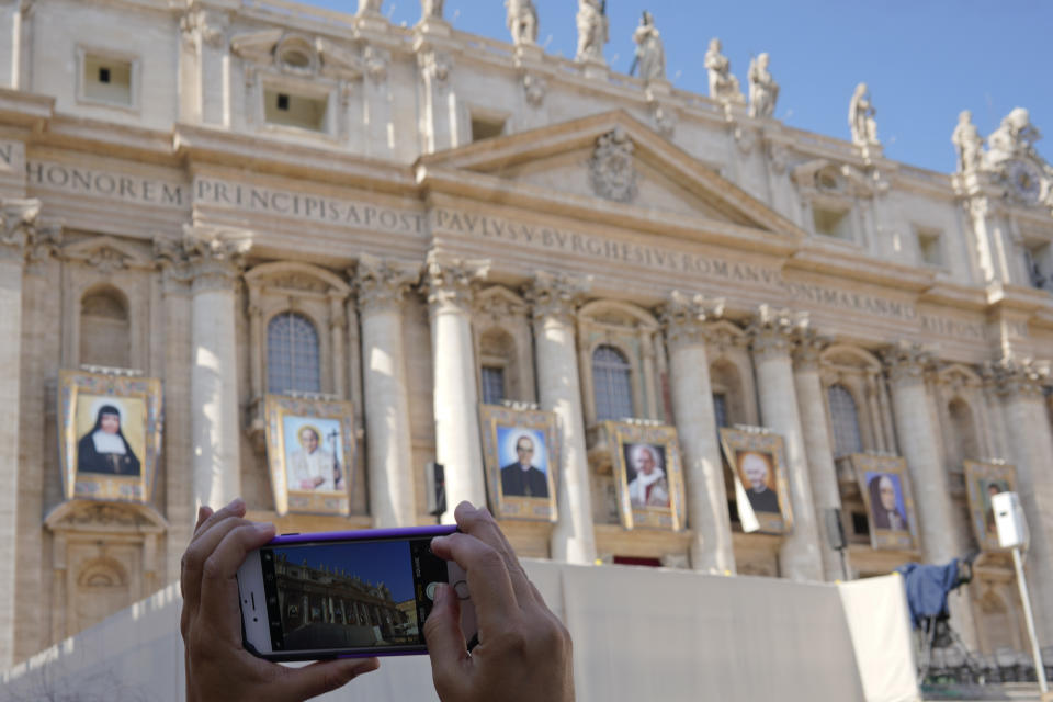 A woman takes photos of tapestries of Roman Catholic Archbishop Oscar Romero, 3rd from left, and Pope Paul VI, 4th from left, hanging from a balcony of the facade of St. Peter's Basilica at the Vatican, Saturday, Oct. 13, 2018. Pope Francis will canonize two of the most important and contested figures of the 20th-century Catholic Church, declaring Pope Paul VI and the martyred Salvadoran Archbishop Oscar Romero as models of saintliness for the faithful today. (AP Photo/Andrew Medichini)