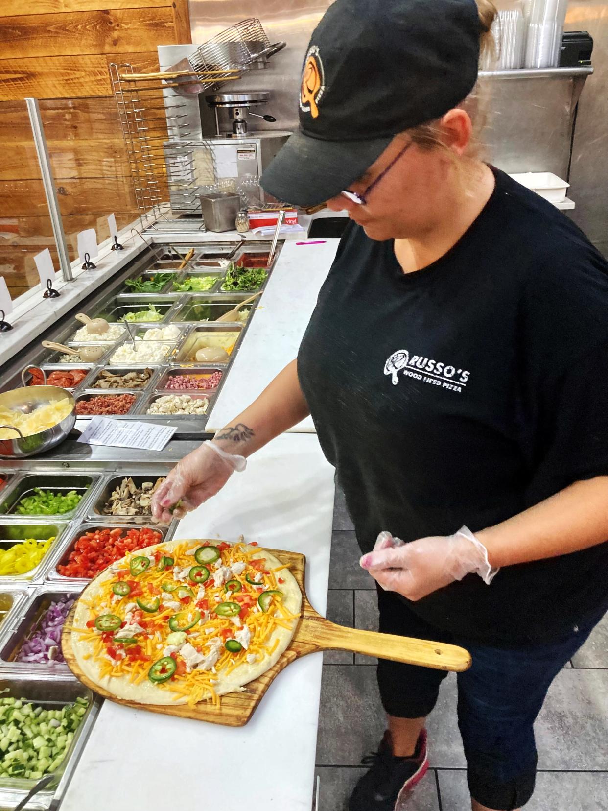 A worker builds the Santa Fe, a specialty item pizza at Russo's Wood Fired Pizza in Zanesville. The restaurant, owned by brothers Anthony and Vincent Russo, is among the many dealing with increased supply costs due to inflation.