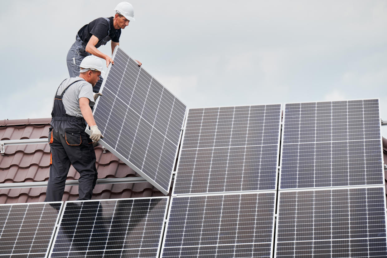 Technicians mounting solar panels on roof of house. (Getty Images)