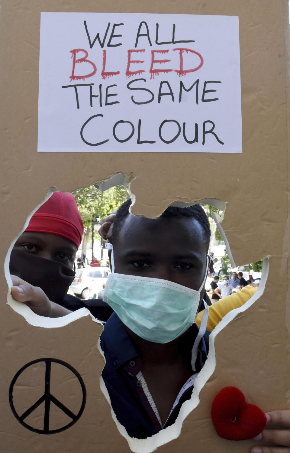 Ein Demonstrant sieht durch eine ausgeschnittene Form mit den Umrissen Afrikas auf einem Schild mit der Aufschrift "We All Bleed The Same Colour" während eines Protests gegen Rassismus und Polizeigewalt. Foto: Hassene Dridi / AP / dpa