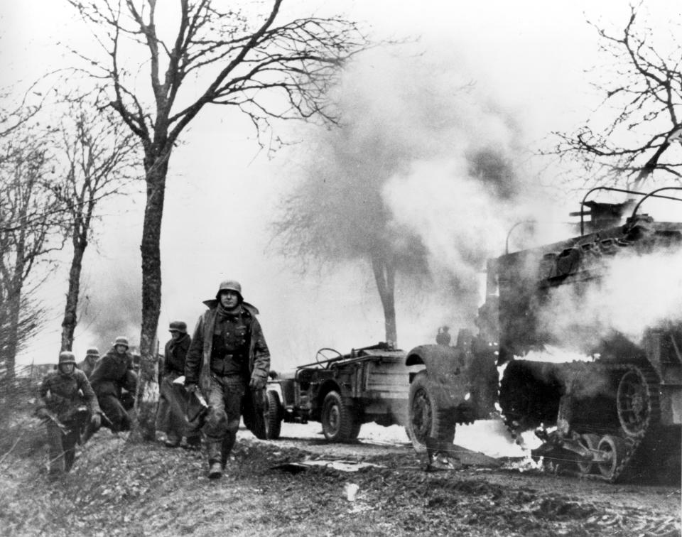 FILE - In this Dec. 1944 file photo, German infantrymen pass by burning captured American vehicles during the drive into Allied lines on the Western Front during the Battle of the Bulge. It was 75 years ago that Hitler launched his last desperate attack to turn the tide for Germany in World War II. At first, German forces drove so deep through the front line in Belgium and Luxembourg that the month-long fighting came to be known as The Battle of the Bulge. When the Germans asked one American commander to surrender, the famous reply came: “Nuts!" By Christmas, American troops had turned the tables on the Germans. Veterans are heading and on Monday, Dec. 16, 2019 when they will mix with royalty and dignitaries to mark perhaps the greatest battle in U.S. military history. (AP Photo, File)