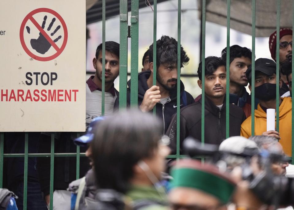 Students watch security personnel guard the main gate of Jamia Millia Islamia university in New Delhi, India, Wednesday, Jan. 25, 2023. Tensions escalated in the university after a student group said it planned to screen a banned documentary that examines Indian Prime Minister Narendra Modi's role during 2002 anti-Muslim riots, prompting dozens of police equipped with tear gas and riot gear to gather outside campus gates. (AP Photo/Manish Swarup)