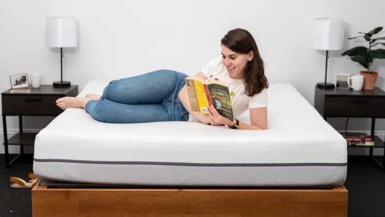 Purple mattress with a woman on top of it in a bedroom setup.