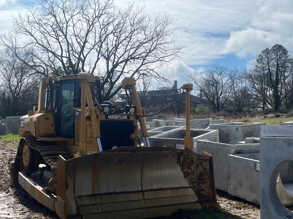 A bulldozer and construction materials sit downhill from an industrial building at the Delaware National housing development east of Hercules Road in Brandywine Hundred in April 2024.