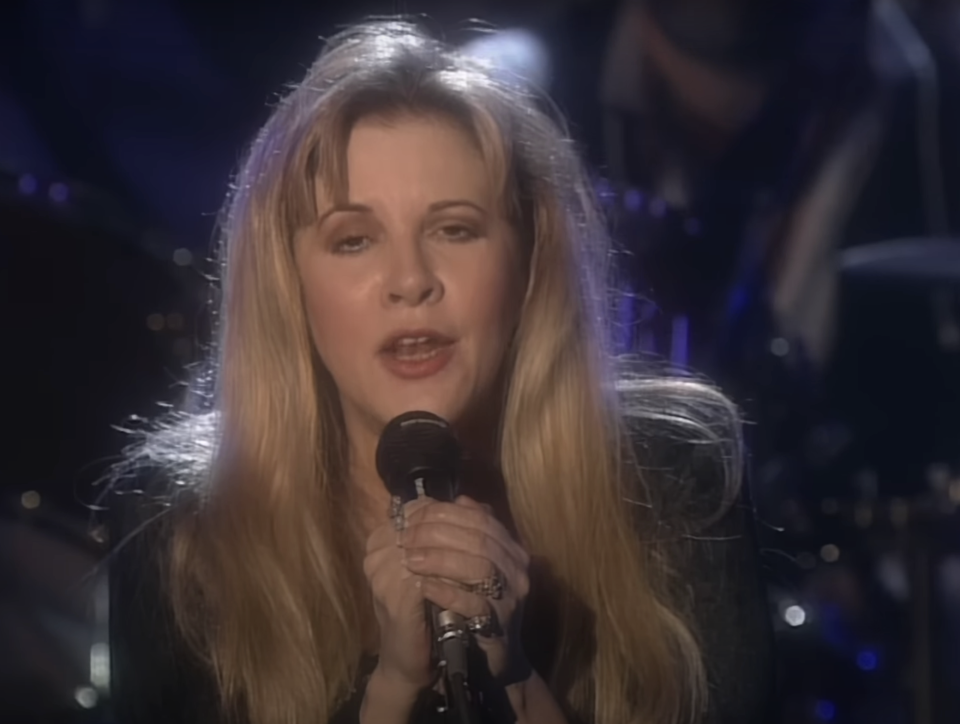 Stevie with long hair singing into a microphone on stage
