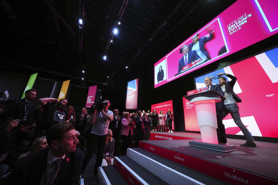 A man jumps on the stage next to Britain's opposition Labour Party leader Keir Starmer during his speech at the Labour Party conference in Liverpool, England, Tuesday, Oct. 10, 2023.(AP Photo/Jon Super)