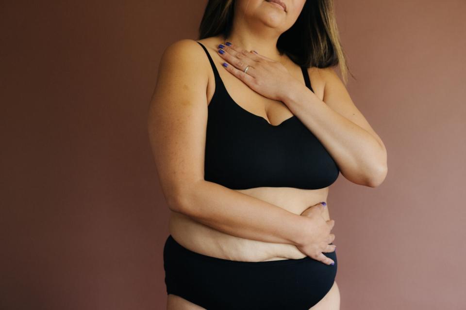 A woman gives herself a hug in black undergarments