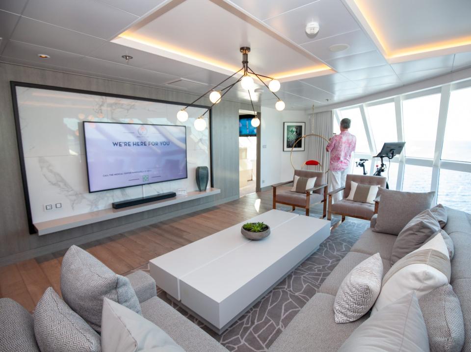 the living room with a large couch facing a TV and a peloton surrounded by windows Iconic suite on the Celebrity Apex cruise ship