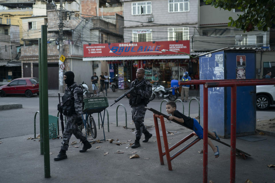 In this July 23, 2019 photo, police officers walk past a child playing on fitness equipment during an operation at the Mare slum complex in Rio de Janeiro, Brazil. The number of police killings has reached the highest levels since records began being kept in 2003. (AP Photo/Leo Correa)